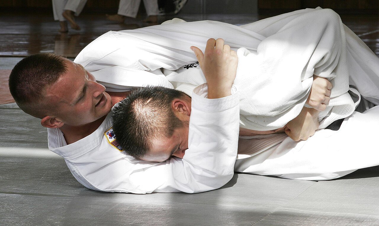 Two practitioners wearing BJJ gis grapple on the mat during a Brazilian jiu-jitsu class